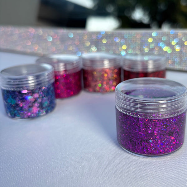 Three containers of glitter on a white surface with a blurred outdoor background