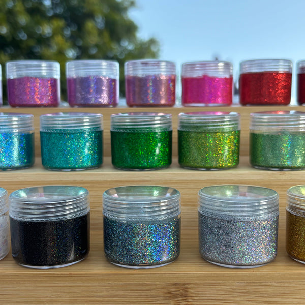 Assorted glitter jars on a wooden stand with a blurred outdoor background
