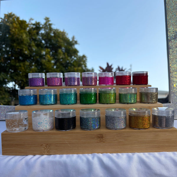 Collection of glitter jars in various colors on a wooden stand with a mirror background.