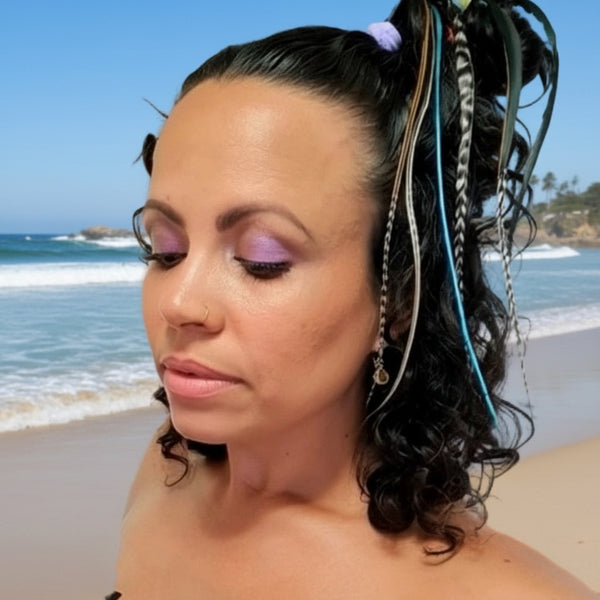 Woman with colorful feathers in hair holding a pink flower, wearing a blue strapless top.