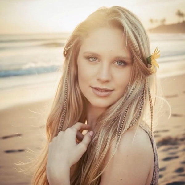 Woman with blonde hair and a flower in her hair on a beach.