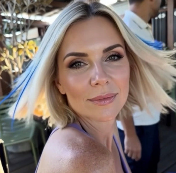 Woman with blonde hair , blue hair feathers and makeup in an outdoor setting