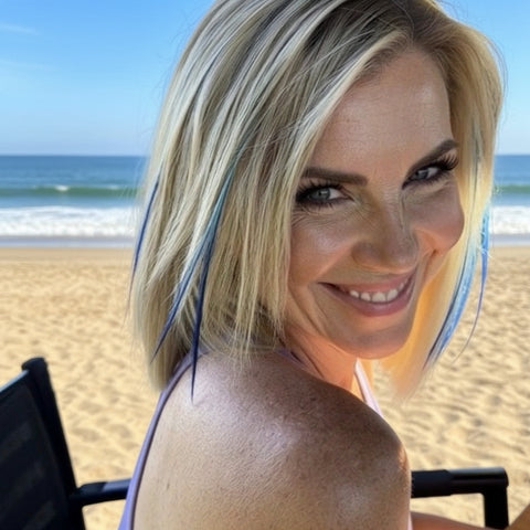Woman with blonde hair , blue skinny hair feathers, smiling outdoors at beach