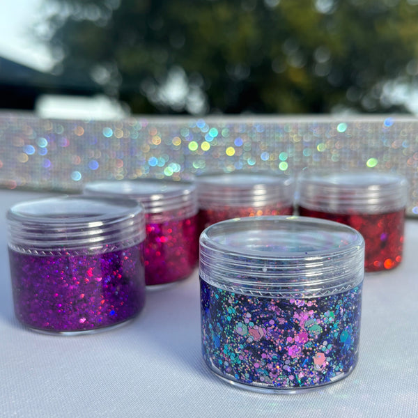 Jars of glitter on a white surface with blurred greenery in the background