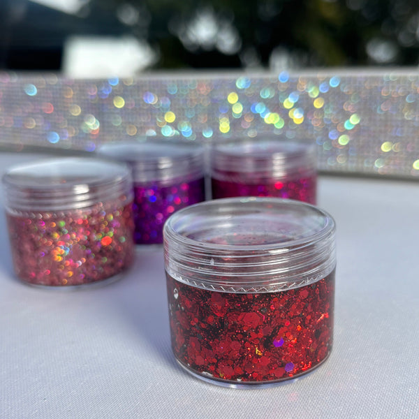 Three small containers of glitter on a reflective surface with a blurred background