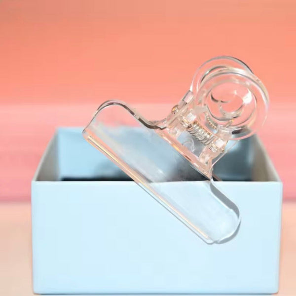 Clear plastic clip on a light blue box with a pinkish-beige background