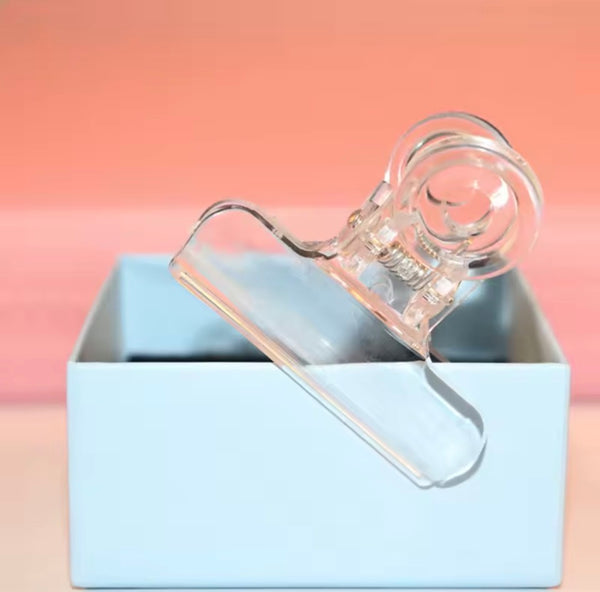 Clear plastic clip on a light blue box with a pinkish-beige background