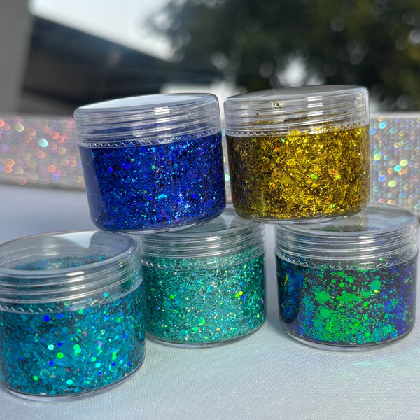 Five small jars of colorful glitter on a light surface with a blurred outdoor background.