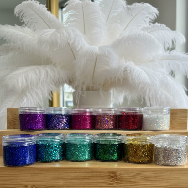 Jars of colorful glitter on a wooden shelf with white feathers in the background