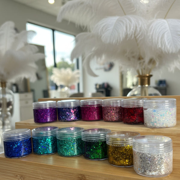 Jars of colorful glitter on a wooden shelf with decorative feathers in the background.
