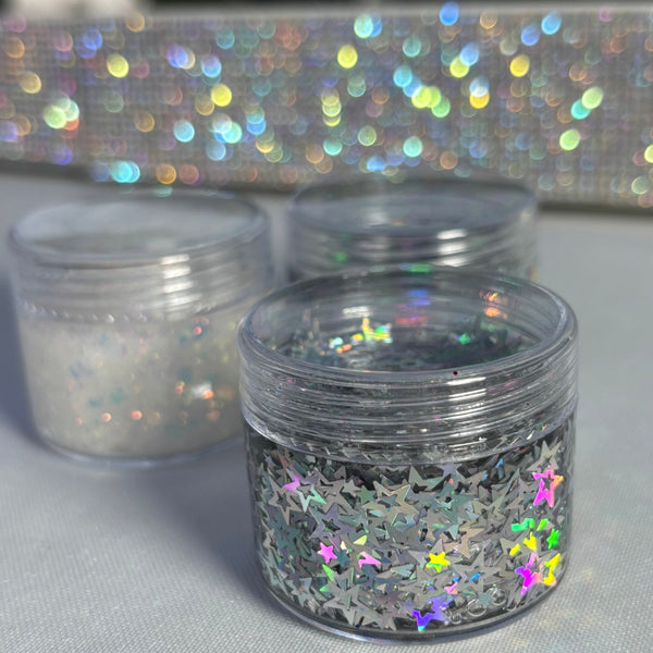 Clear containers with colorful glittery contents on a gray surface with a sparkly background.