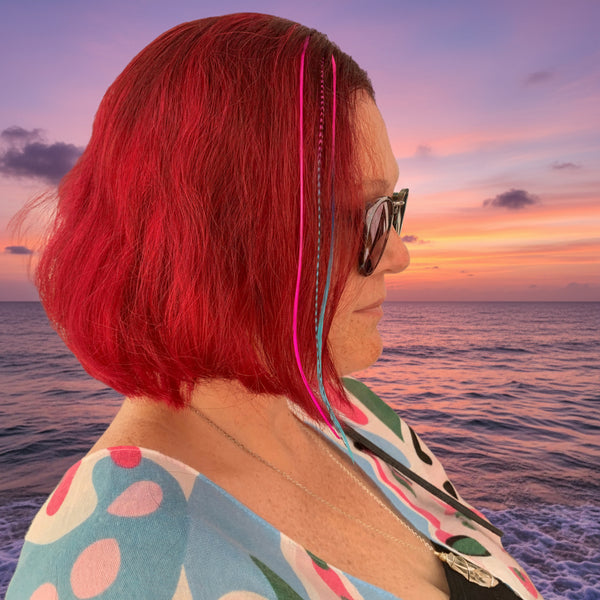 Woman with red hair and sunglasses in front of a display of colorful hair extensions.