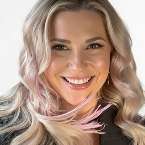 Woman with light pink hair feathers smiling in front of a blurred cityscape background