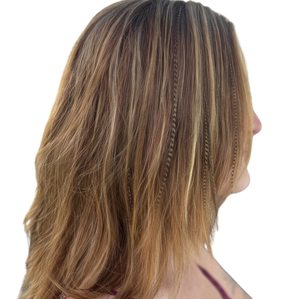 Close-up of a person with brown, wavy hair wearing fawn grizzly feather extensions on a white background
