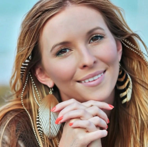 Woman with long hair and feathered earrings against a blurred natural background