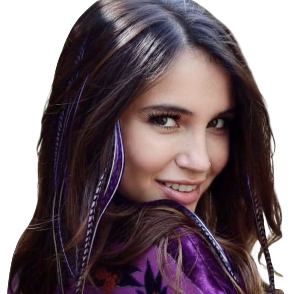 Woman with long brown hair wearing purple feather extensions, with floral pattern top, outdoors.