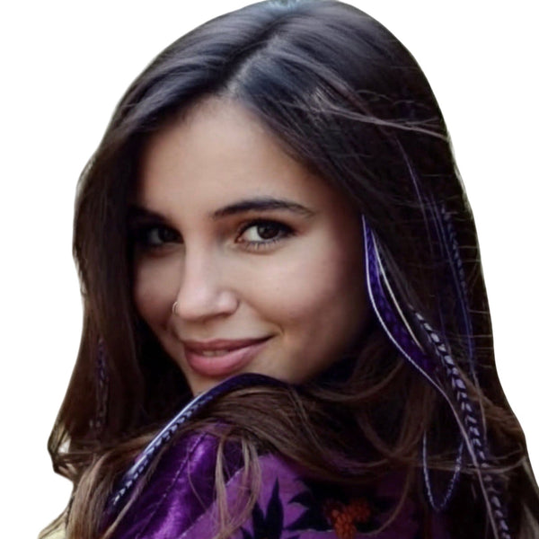 Woman with long brown hair wearing purple feather extensions smiling outdoors.