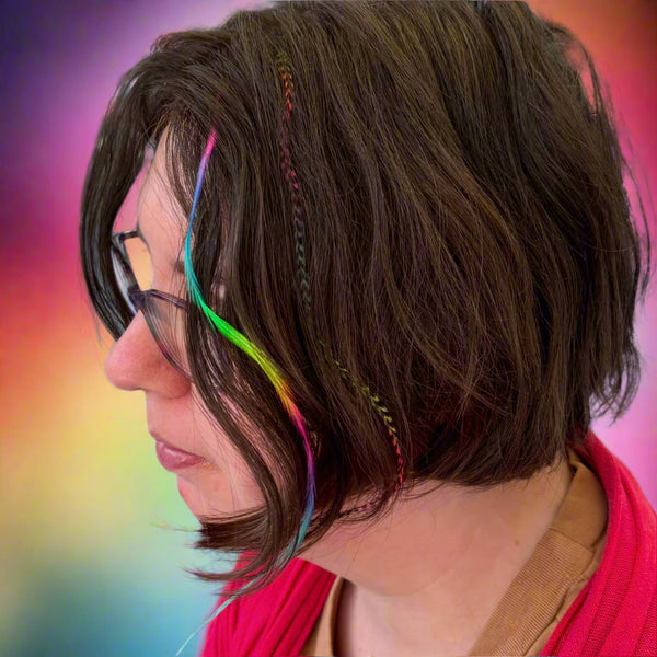 Person with short brown hair featuring rainbow strands, wearing glasses, in an outdoor setting.