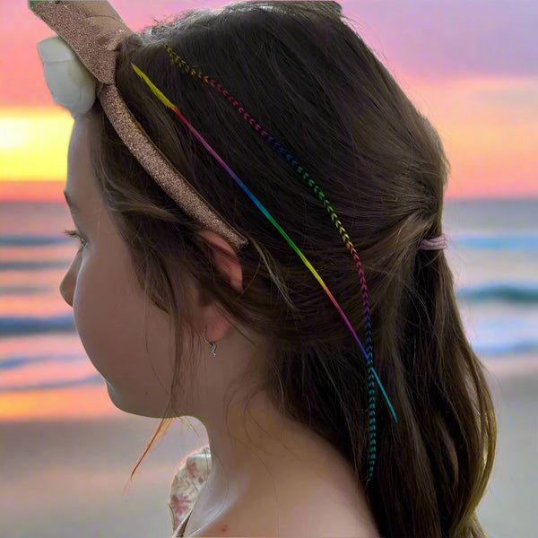 Person with rainbow feather hair extensions in their hair at the beach