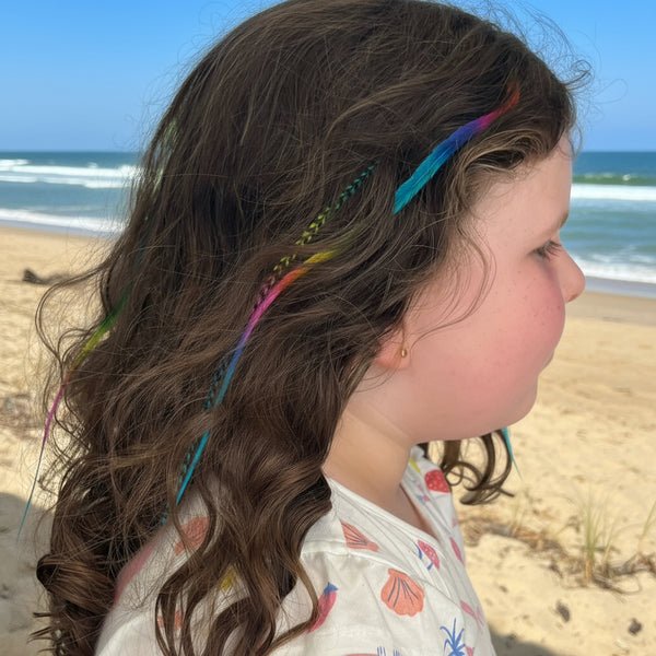 Girl with colourful rainbow feather hair extension accessories in a wavy hairstyle, outdoors.