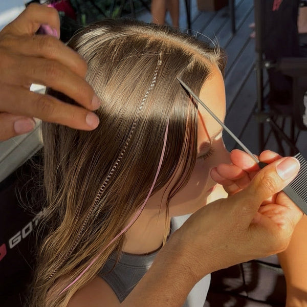 Person getting a hair extension styled by another person in a salon setting.