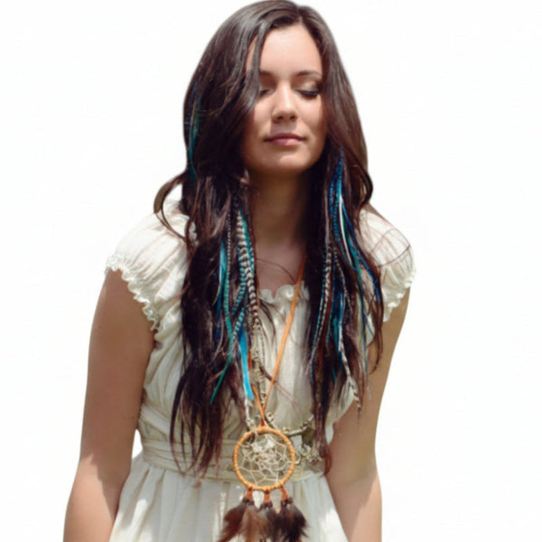 Woman with long hair and a dreamcatcher necklace standing in a field with greenery and flowers.