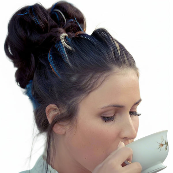 Woman with styled blue hair feathers hairstyle sipping from a teacup against a white background