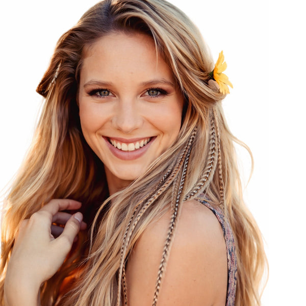 Woman with long blonde hair, wearing natural ginger grizzly feather hair extensions by Wild4Feathers and a yellow flower in her hair on a white background