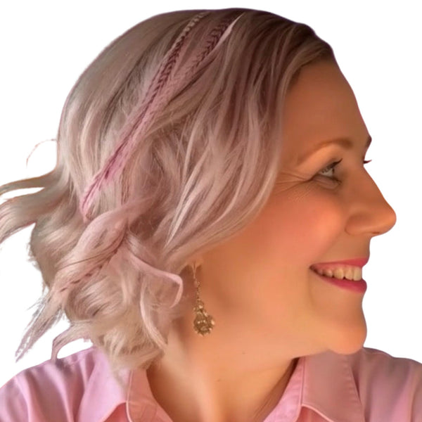 Woman with blonde styled hair wearing light pink feather hair extensions against a sunset beach background