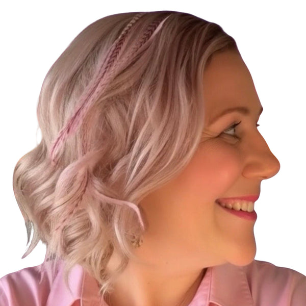 Woman with styled blonde hair wear light pink feather hair extensions against a sunset beach backdrop