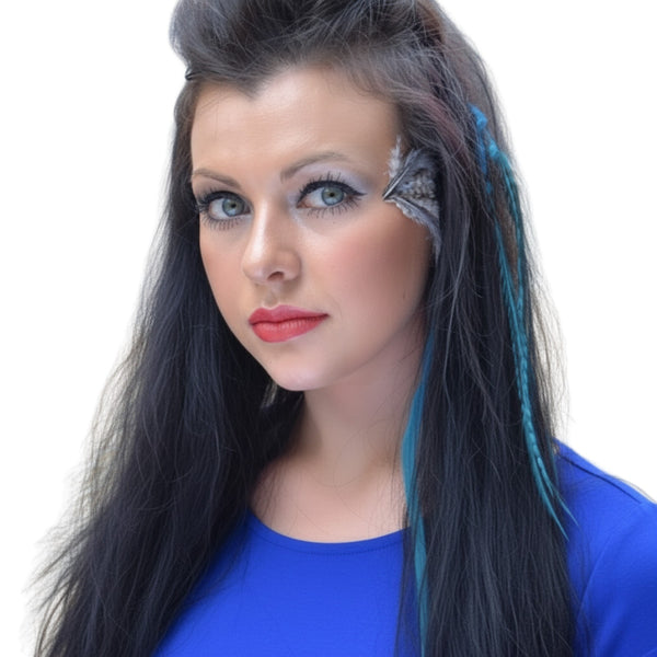 Woman with blue feathers in hair and makeup wearing a blue top on a white background