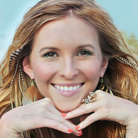 Woman with long blonde hair and a bright smile, wearing a headband and necklace.